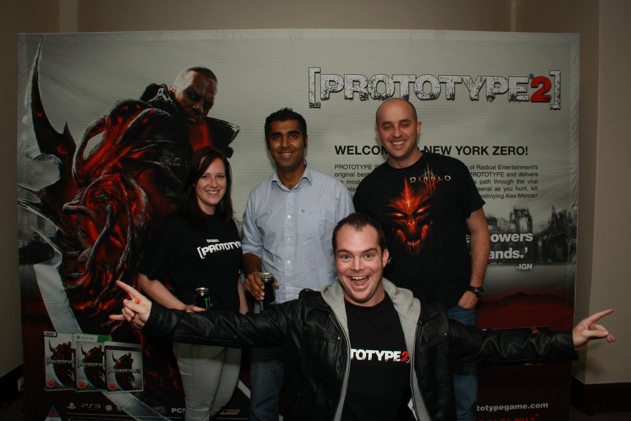 Devon pointing at the camera with three colleagues in front of a Prototype 2 banner